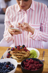 Young woman using smartphone at breakfast - ABIF00934