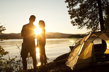 Zwei junge Erwachsene lachen und lächeln bei Sonnenuntergang auf einem Camping- und Kajakausflug in Idaho. - AURF01594