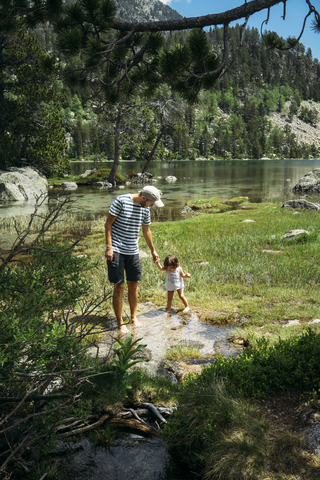 Spanien, Vater und Tochter erkunden einen Bergsee, stehen knöcheltief im Wasser, lizenzfreies Stockfoto