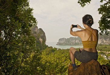 Frau fotografiert mit ihrem Smartphone auf einem Aussichtspunkt über dem Railay-Strand - AURF01646