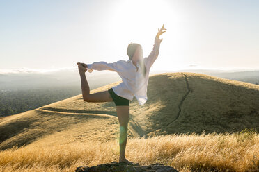 Frau in Yogastellung in einem Feld mit goldenem Gras in den sonnenverwöhnten Hügeln Kaliforniens. - AURF01653