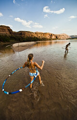 Two women playing and hula hooping in a shallow river. - AURF01668