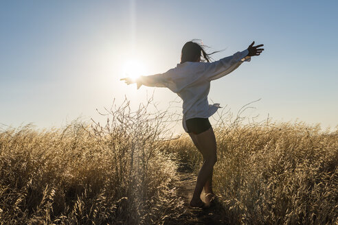Eine Frau tanzt in einem Feld mit goldenem Gras in den sonnenverwöhnten Hügeln Kaliforniens. - AURF01734