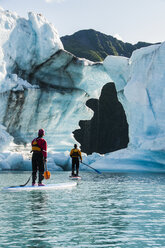 Zwei Erwachsene auf Stand Up Paddle Boards (SUP) beobachten das geschmolzene Loch im Eisberg auf dem Bear Lake im Kenai Fjords National Park, Alaska. - AURF01763