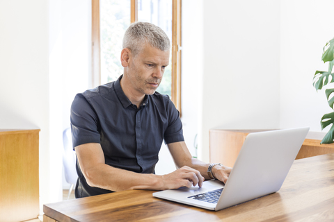 Älterer Mann mit Laptop auf Holztisch, lizenzfreies Stockfoto