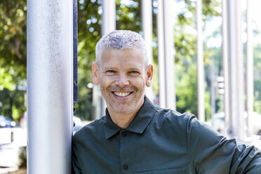 Portrait of a smiling mature man leaning against a pole - TCF05690