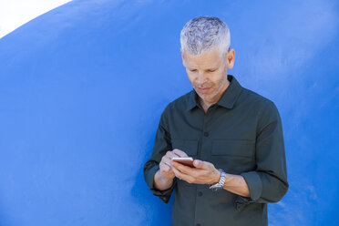 Älterer Mann benutzt Handy an einer blauen Wand - TCF05701