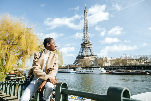 France, Paris, Smiling woman at river Seine with the Eiffel Tower in the background - KIJF02000