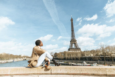Frankreich, Paris, Frau sitzt auf Brücke über die Seine und schaut auf Eiffelturm - KIJF02008