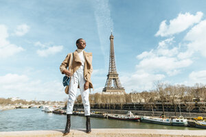 Frankreich, Paris, Lächelnde Frau auf einer Brücke stehend mit dem Eiffelturm im Hintergrund - KIJF02013