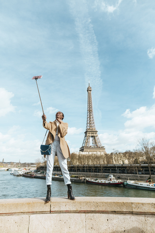 Frankreich, Paris, Frau steht auf Brücke über die Seine mit dem Eiffelturm im Hintergrund und macht ein Selfie, lizenzfreies Stockfoto