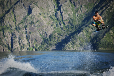 Ein sportlicher männlicher Wakeboarder fährt bei Sonnenuntergang auf einem See in Idaho über das Kielwasser. - AURF01914