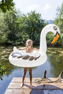 Happy girl standing on jetty at a pond with inflatable pool toy in swan shape - TCF05722