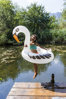 Carefree girl jumping into pond with inflatable pool toy in swan shape - TCF05723