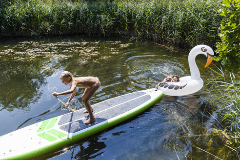 Two girls in a pond with inflatable pool toy in swan shape and SUP board - TCF05728