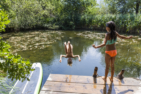 Mädchen beobachtet ihre Freundin beim Sprung in den Teich, lizenzfreies Stockfoto