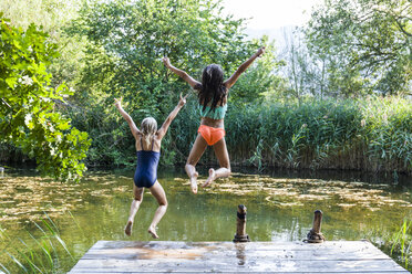 Two carefree girls jumping into pond - TCF05734