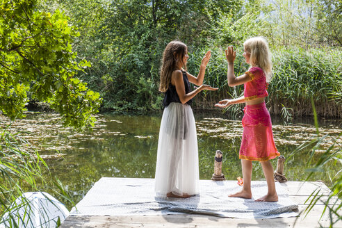 Zwei Mädchen in schicken Kleidern stehen auf einem Steg an einem Teich und klatschen in die Hände - TCF05742