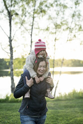 Finland, Kuopio, mother carrying daughter piggyback at a lake - PSIF00028