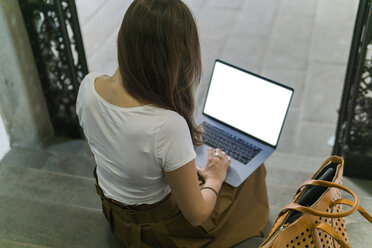 Frau sitzt auf einer Treppe und benutzt einen Laptop - FBAF00009