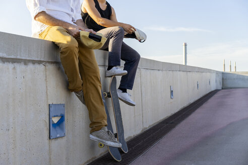 Nahaufnahme von zwei jungen Männern mit Skateboards, die auf einer Mauer sitzen - AFVF01481