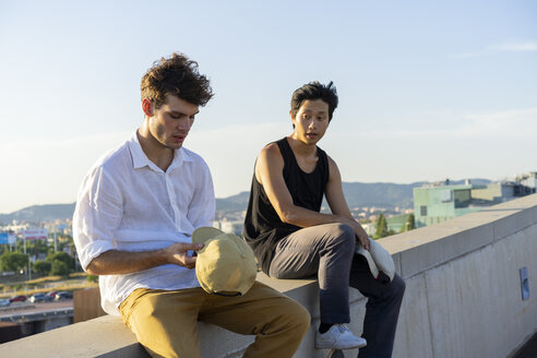 Zwei junge Männer sitzen und sprechen an einer Wand - AFVF01482