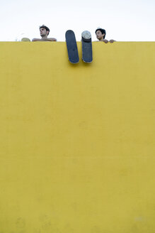 Zwei junge Männer mit Skateboards hinter einer hohen gelben Mauer schauen sich um - AFVF01501