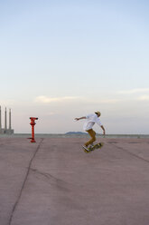 Junger Mann macht einen Skateboardtrick auf einer Fahrbahn in der Abenddämmerung - AFVF01507