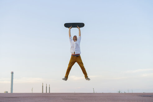 Young man jumping in the air holding a skateboard - AFVF01508