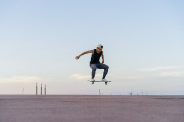 Young man doing a skateboard trick on a lane at dusk - AFVF01510