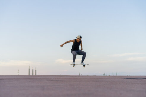 Junger Mann macht einen Skateboardtrick auf einer Fahrbahn in der Abenddämmerung - AFVF01510