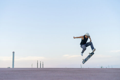 Junger Mann macht einen Skateboardtrick auf einer Fahrbahn in der Abenddämmerung - AFVF01513