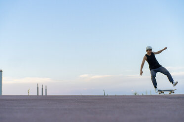 Young man doing a skateboard trick on a lane at dusk - AFVF01518