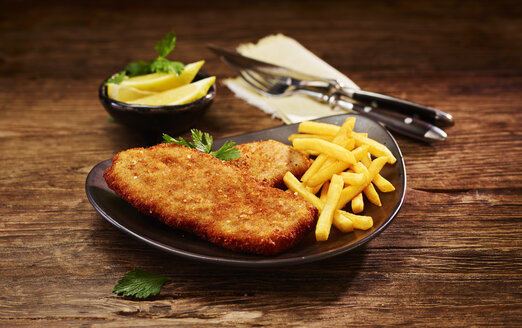 Schweineschnitzel und Pommes frites auf dem Teller, Zitrone in der Schale - KSWF01973