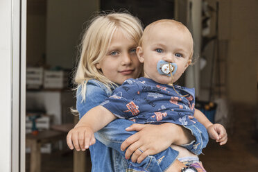 Portrait of girl holding baby boy brother at home - TCF05764