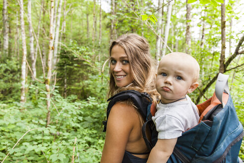 Porträt einer lächelnden Mutter beim Wandern im Wald mit einem kleinen Jungen im Rucksack - TCF05767