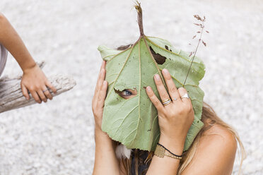 Playful woman peeking through hole in large leaf - TCF05770