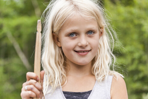 Porträt eines lächelnden Mädchens, das einen Holzstab im Freien hält - TCF05772