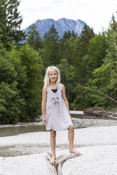 Portrait of smiling girl standing on dead wood at the riverside - TCF05773