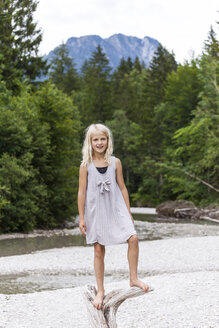 Porträt eines lächelnden Mädchens, das auf Totholz am Flussufer steht - TCF05773