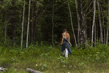 Rückansicht einer Frau, die mit Pfeil und Bogen durch einen Wald läuft - TCF05789