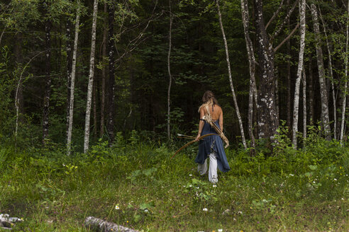 Rückansicht einer Frau, die mit Pfeil und Bogen durch einen Wald läuft - TCF05789