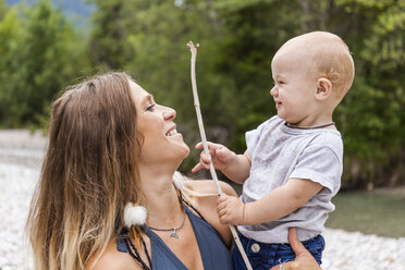 Lächelnde Mutter mit einem kleinen Jungen, der einen Stock in der Natur hält - TCF05795