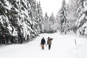 Italien, Modena, Cimone, Paar mit Skifahrern und Snowboard im Winterwald unterwegs - JPIF00008