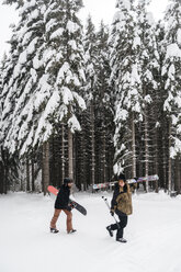 Italien, Modena, Cimone, Paar mit Skifahrern und Snowboard im Winterwald unterwegs - JPIF00010