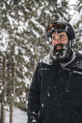 Lächelnder junger Mann in Skikleidung im Winterwald mit Blick zur Seite - JPIF00017