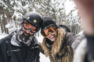 Selfie eines lächelnden Paares in Skikleidung im Winterwald - JPIF00023