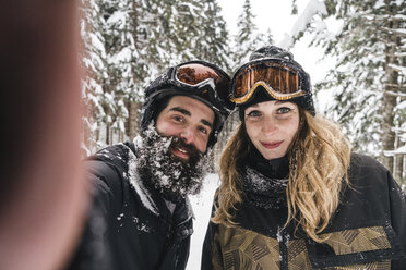 Selfie eines lächelnden Paares in Skikleidung im Winterwald - JPIF00024