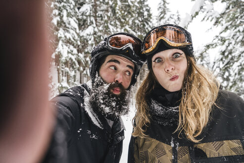 Selfie eines glücklichen Paares in Skikleidung, das im Winterwald Grimassen schneidet - JPIF00025