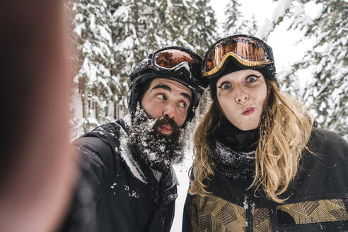 Selfie of happy couple in skiwear grimacing in winter forest - JPIF00025